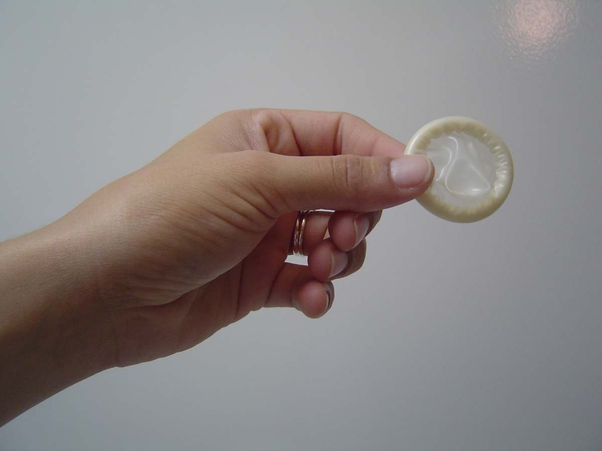 fota de uma mão feminina segurando um preservativo.
