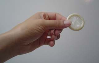 fota de uma mão feminina segurando um preservativo.